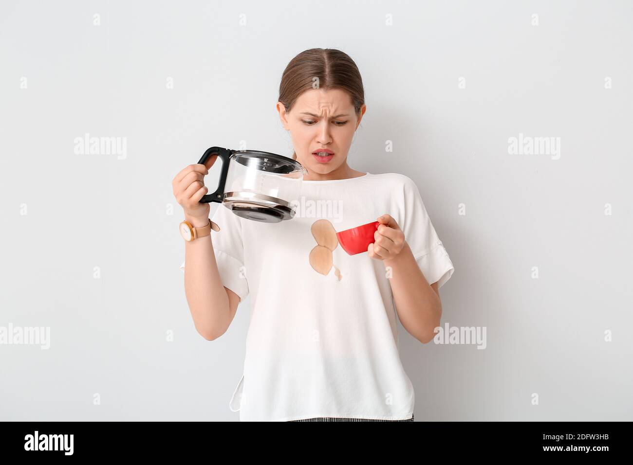Giovane donna stressata con macchie di caffè sulla sua t-shirt sfondo bianco Foto Stock