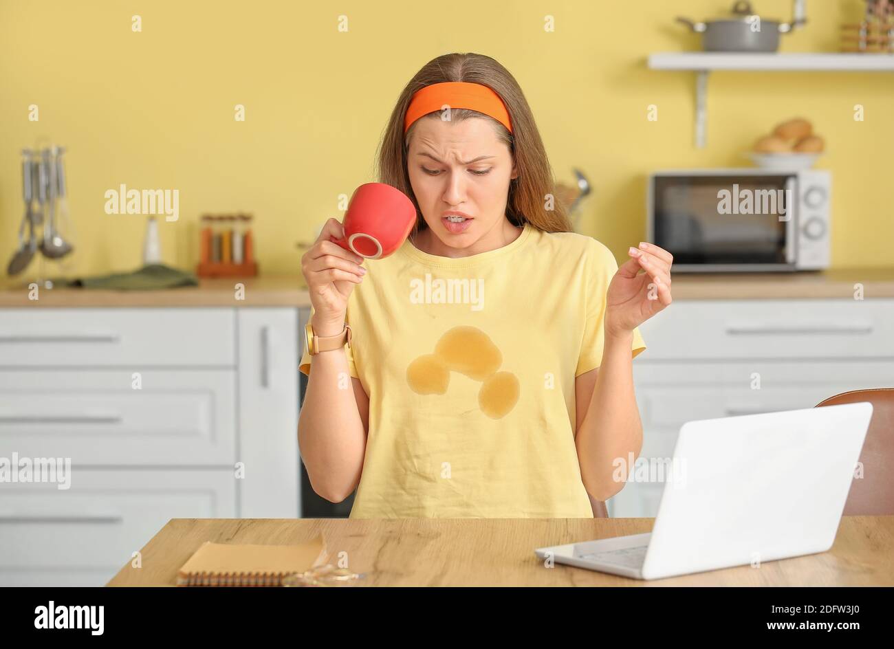 Giovane donna stressata con macchie di caffè sulla sua t-shirt dentro cucina Foto Stock