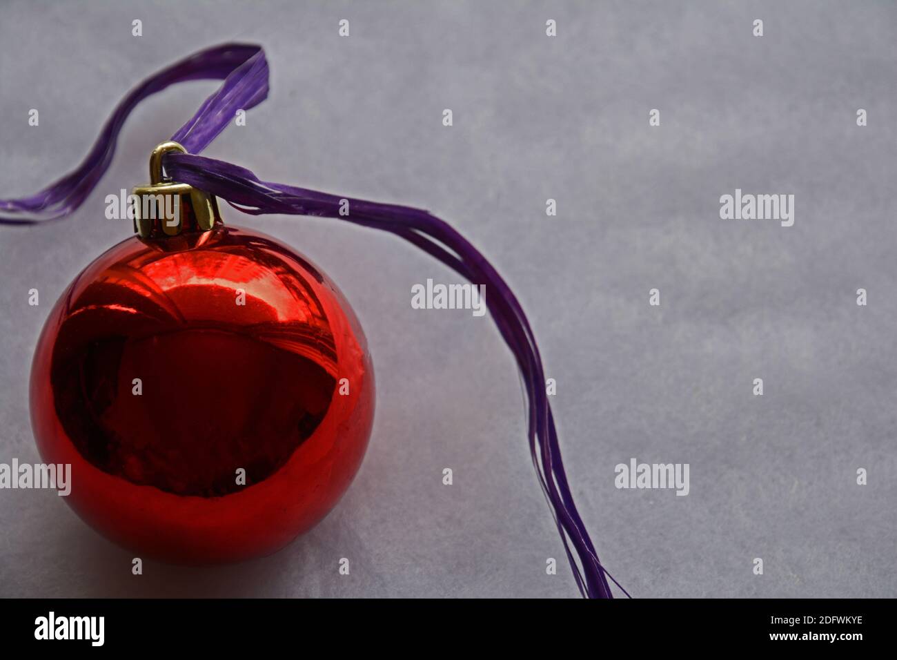 Un grande ornamento rosso natalizio palla con nastro viola su sfondo grigio con spazio per la copia. Foto Stock