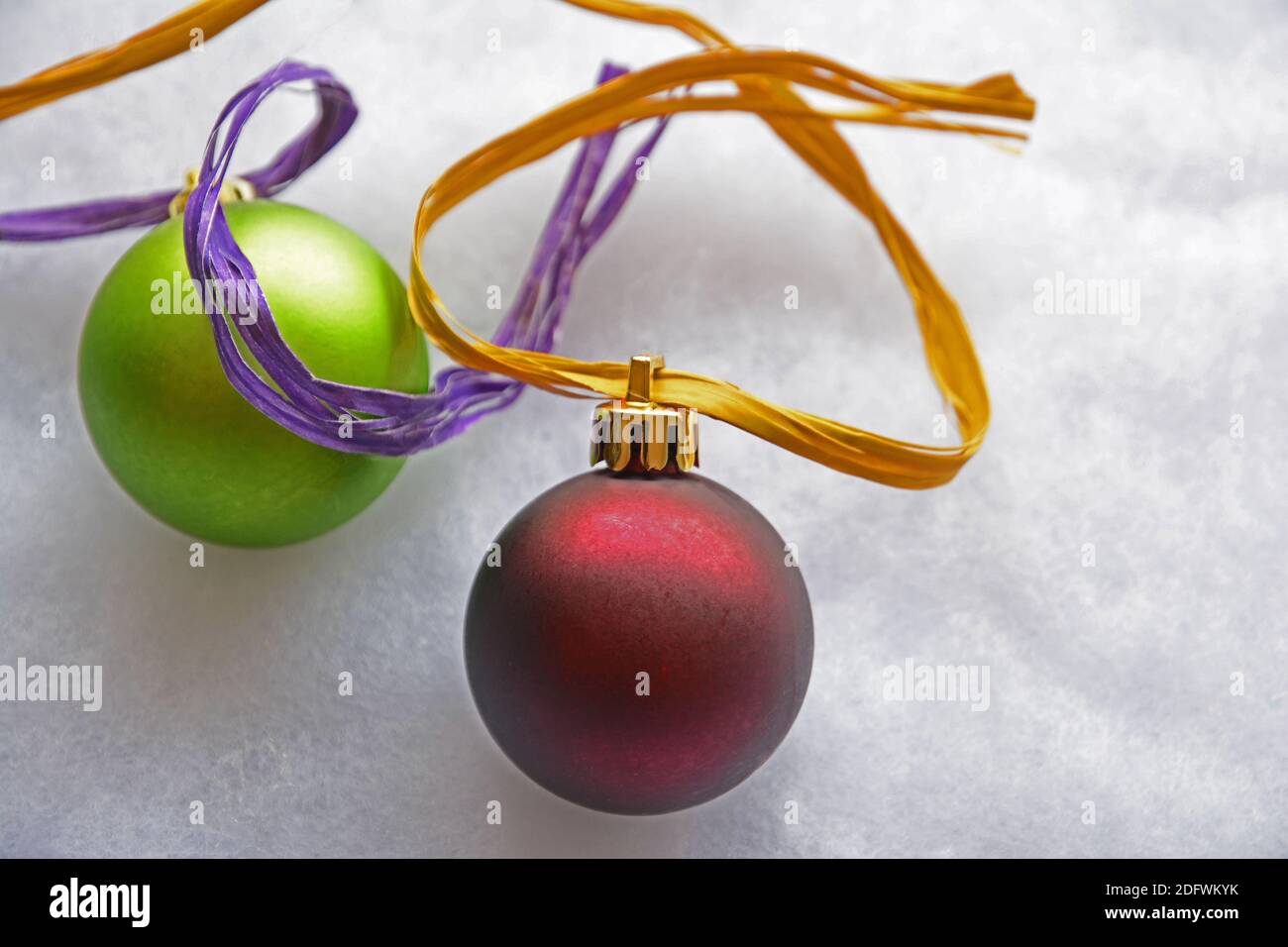 Un rosso e un verde grande Natale palla ornamenti con oro e nastro viola su sfondo grigio. Foto Stock