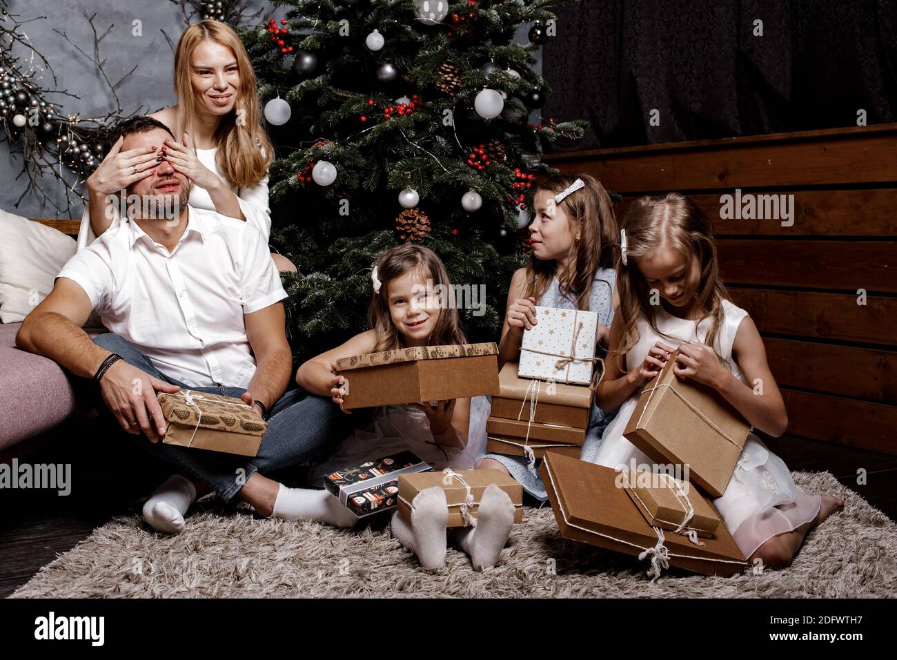Felice famiglia carina con tre bambini che scambiano regali sotto l'albero di Natale sul tappeto. Concetto di famiglia e vacanza. Foto Stock