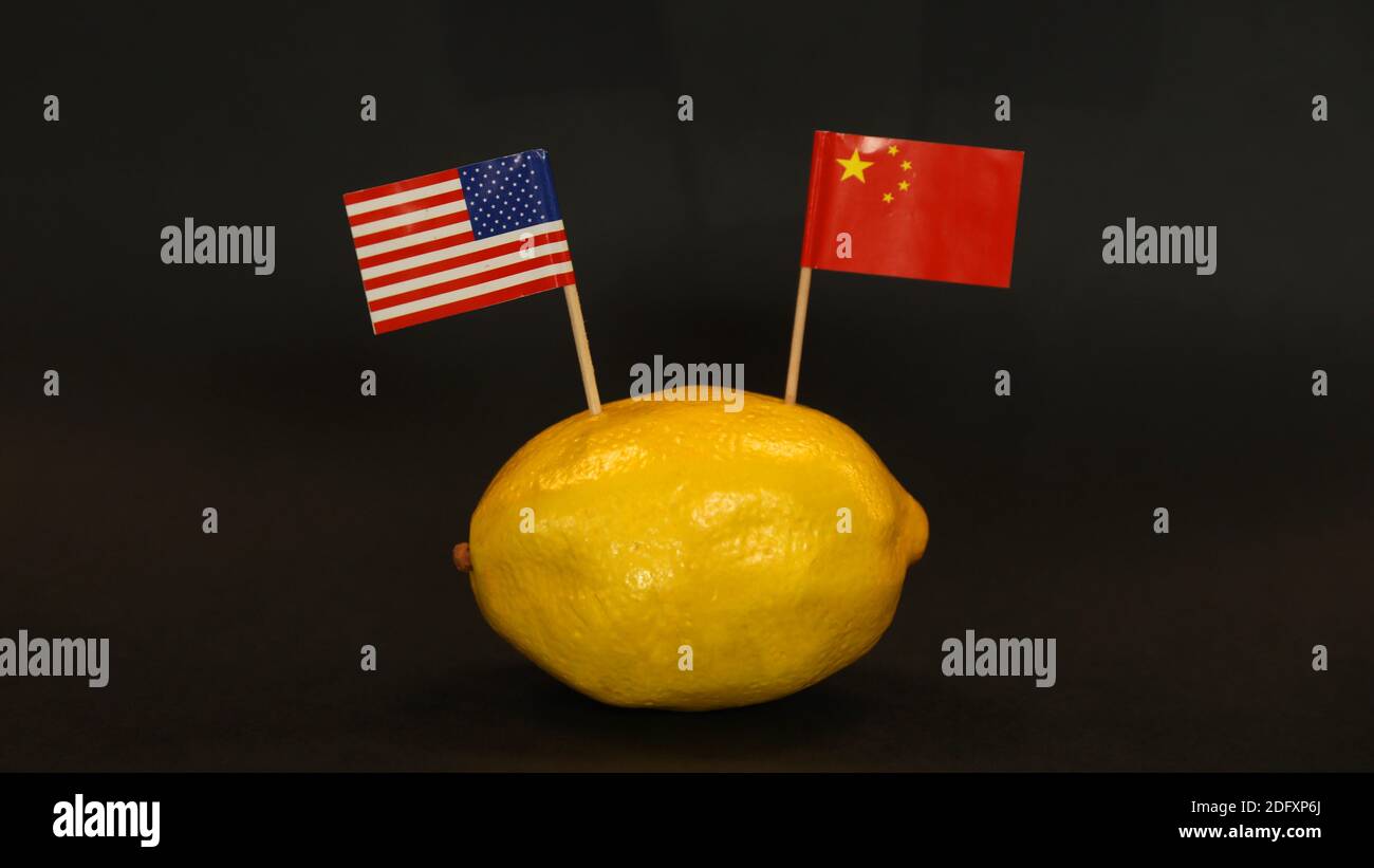 Le bandiere nazionali DEGLI STATI UNITI e dei Cinesi si sono bloccate nella pelle di un limone giallo brillante. Simbolo delle relazioni internazionali soured, strained, amaro, teso. Foto Stock