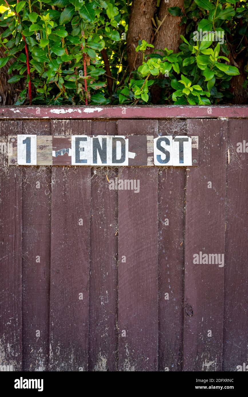 Un indirizzo rotto che ora recita '1 End Street' che potrebbe rappresentare una fine delle cose. Bruna recinzione sporca con foglie e ciottoli, verticale Foto Stock