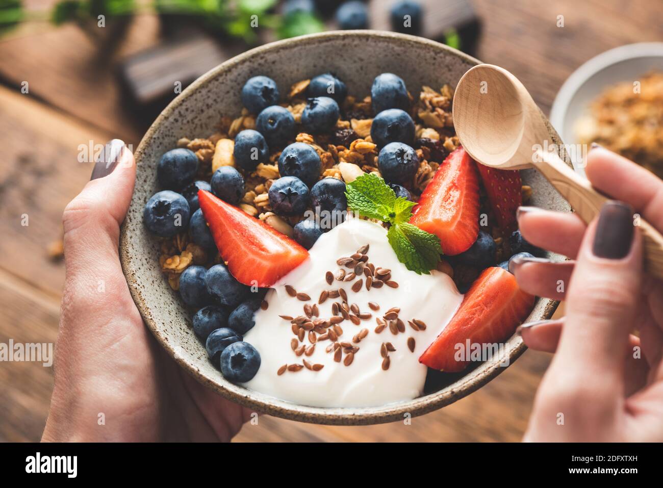 Ciotola di granola con frutta e yogurt greco in mani femminili. Menu di cibo fitness, dieta, concetto di cibo pulito Foto Stock