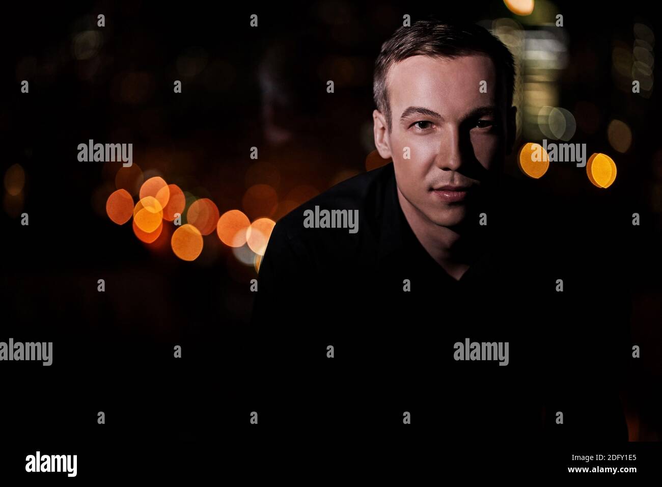 Ritratto di un bel giovane sicuro su uno sfondo nero sfocato all'esterno con spazio di copia, guarda la fotocamera Foto Stock