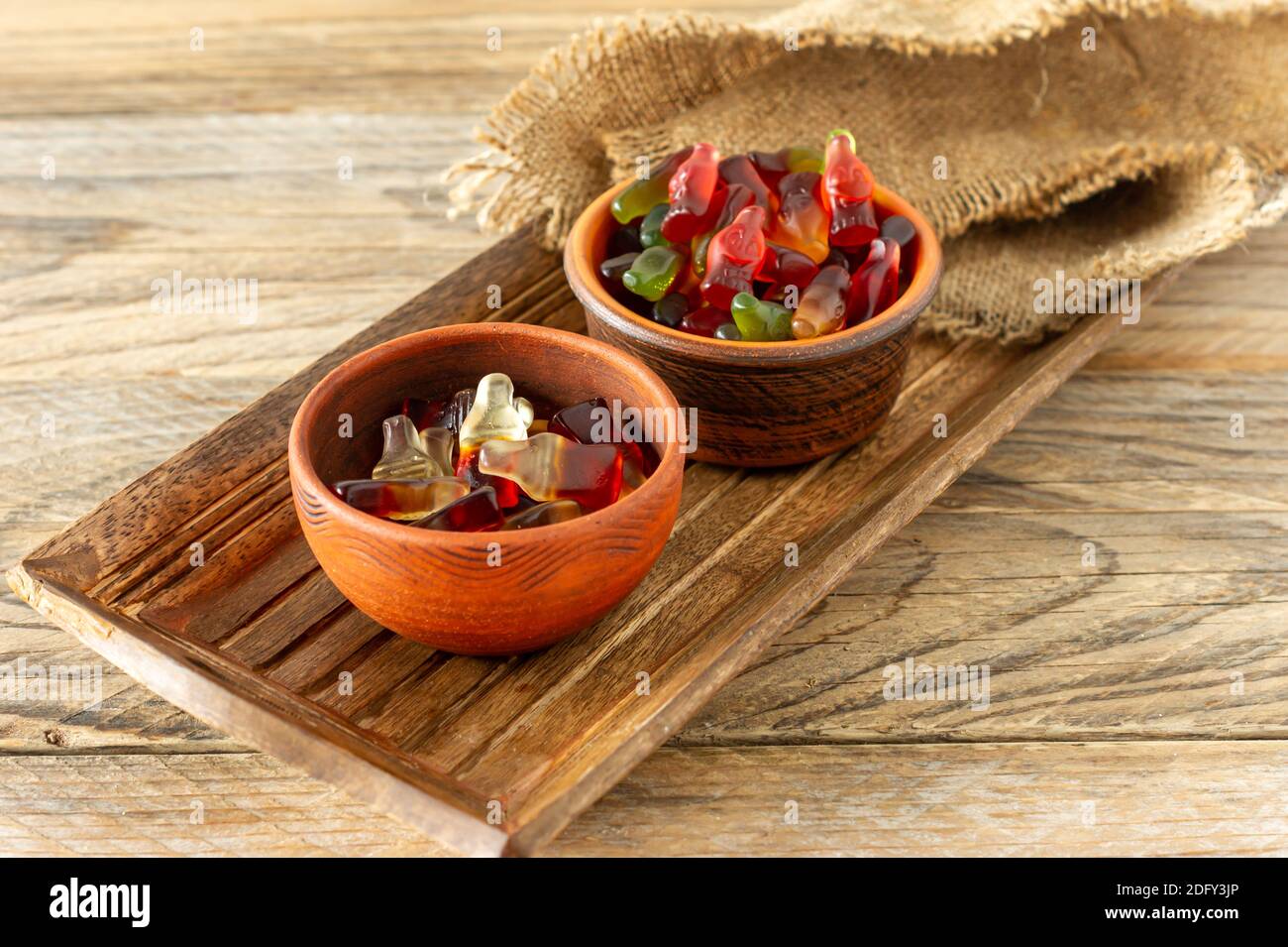 caramelle colorate e caramelle dolci, gelatina caramelle sapore frutta, dolci caramelle in ciotole di argilla in stile rustico vassoio di legno Foto Stock