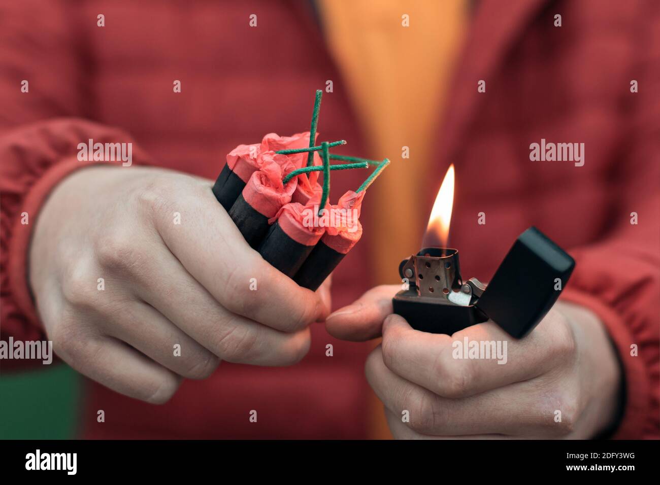 Uomo in rosso jacked illuminazione di diversi Firecrackers in mano con accendino a benzina. Guy prepararsi per il divertimento di Capodanno con fuochi d'artificio o prodotti pirotecnici Foto Stock