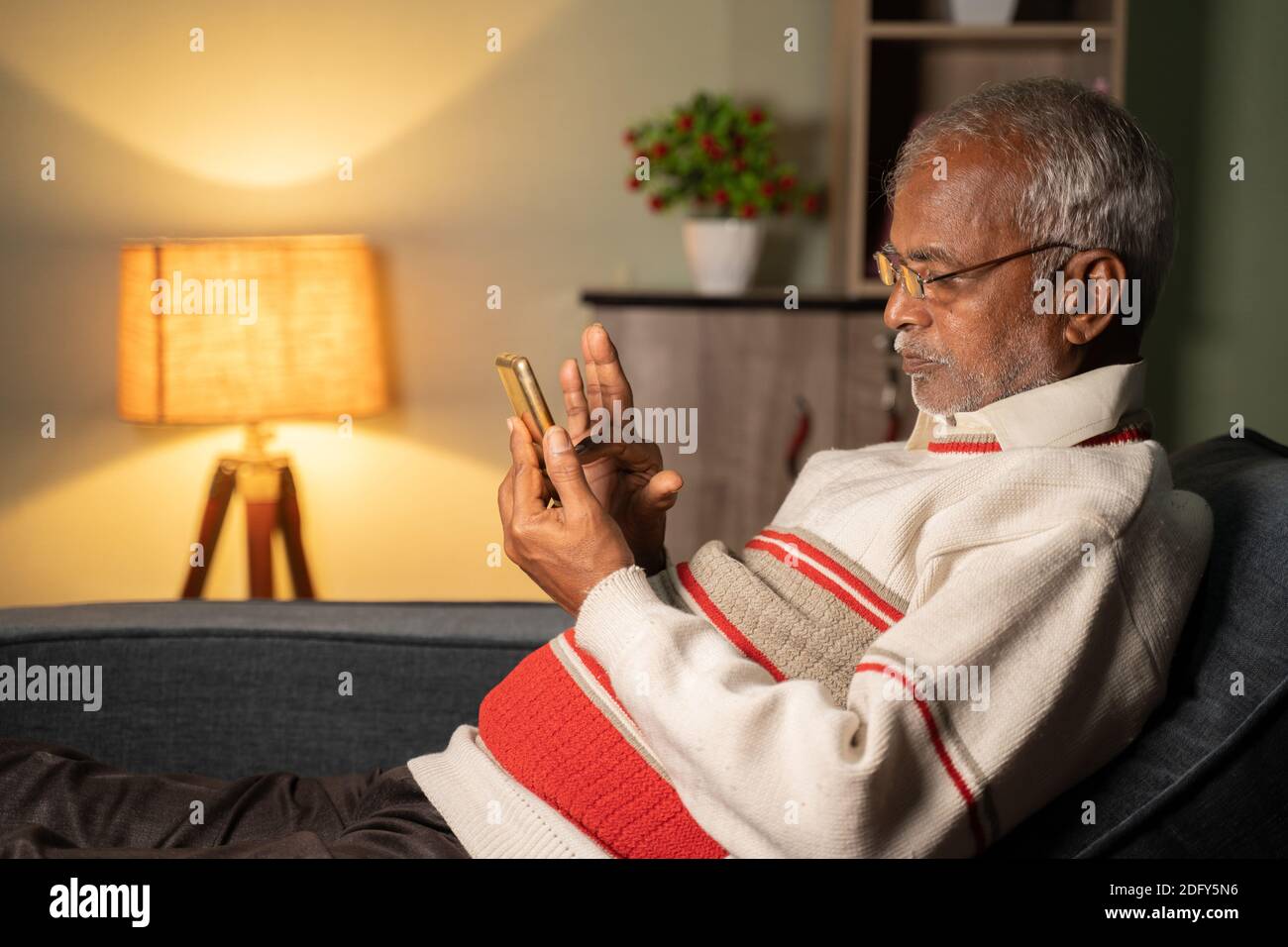 Anziano impegnato a utilizzare il telefono cellulare a casa mentre dormiva sul divano - concetto di anziani che utilizzano tecnologia, Internet e social media Foto Stock