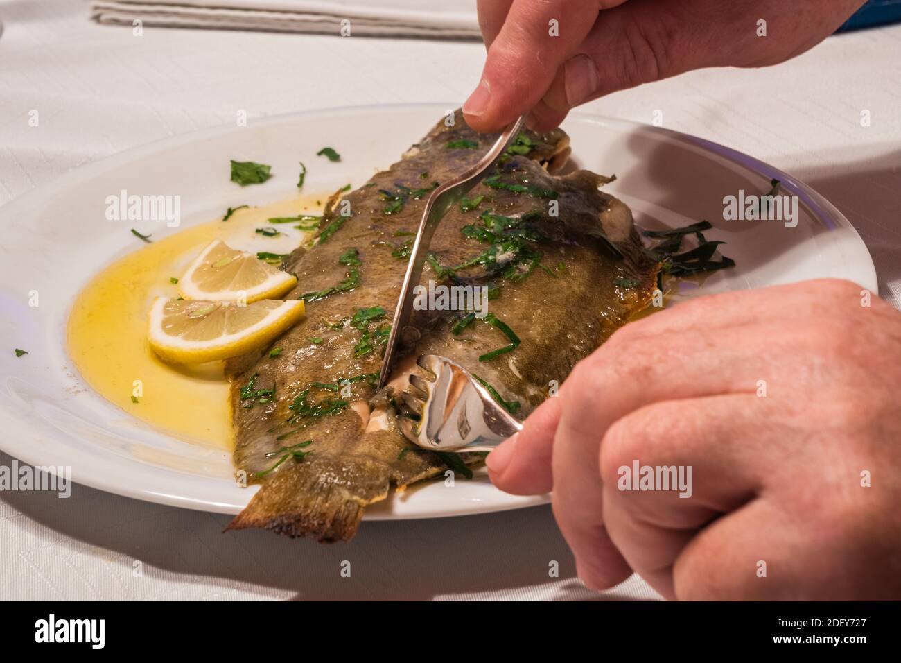 Filetto o consumo di Suola Meuniere con burro marrone, prezzemolo e limone su un piatto bianco con forchetta e coltello per il pesce Foto Stock