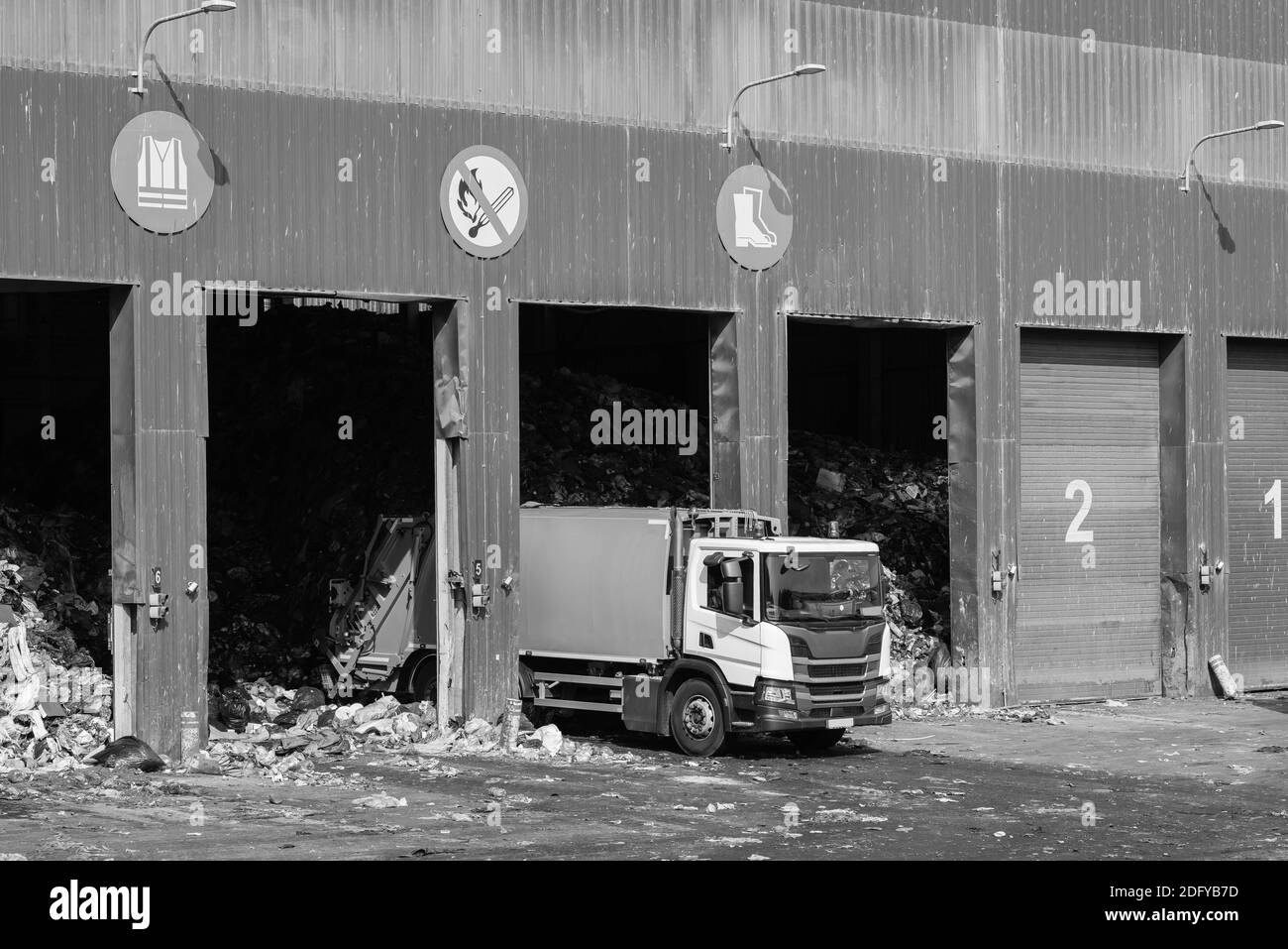 Camion per rifiuti bianchi che scaricano i rifiuti in magazzino. Smistamento dei rifiuti. Riciclaggio. Attenzione all'ambiente. Bianco e nero. Foto Stock