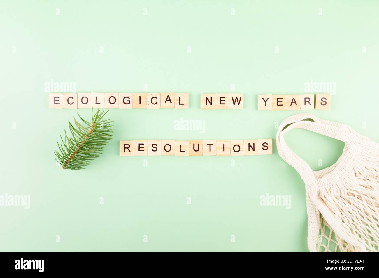 Frase 'risoluzioni ecologiche del nuovo anno' in lettere di legno su sfondo verde, borsa a corda e rami di abete Foto Stock