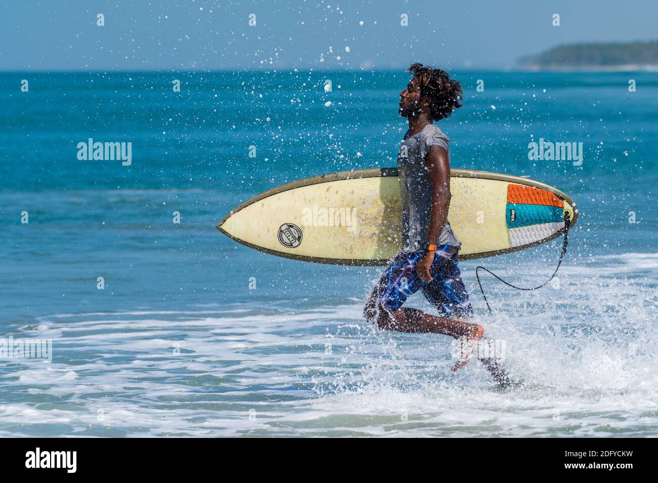 VARKALA, INDIA - Mar 14, 2020: Un surfer indiano maschio che corre furiousltowards l'oceano per catturare le onde Foto Stock