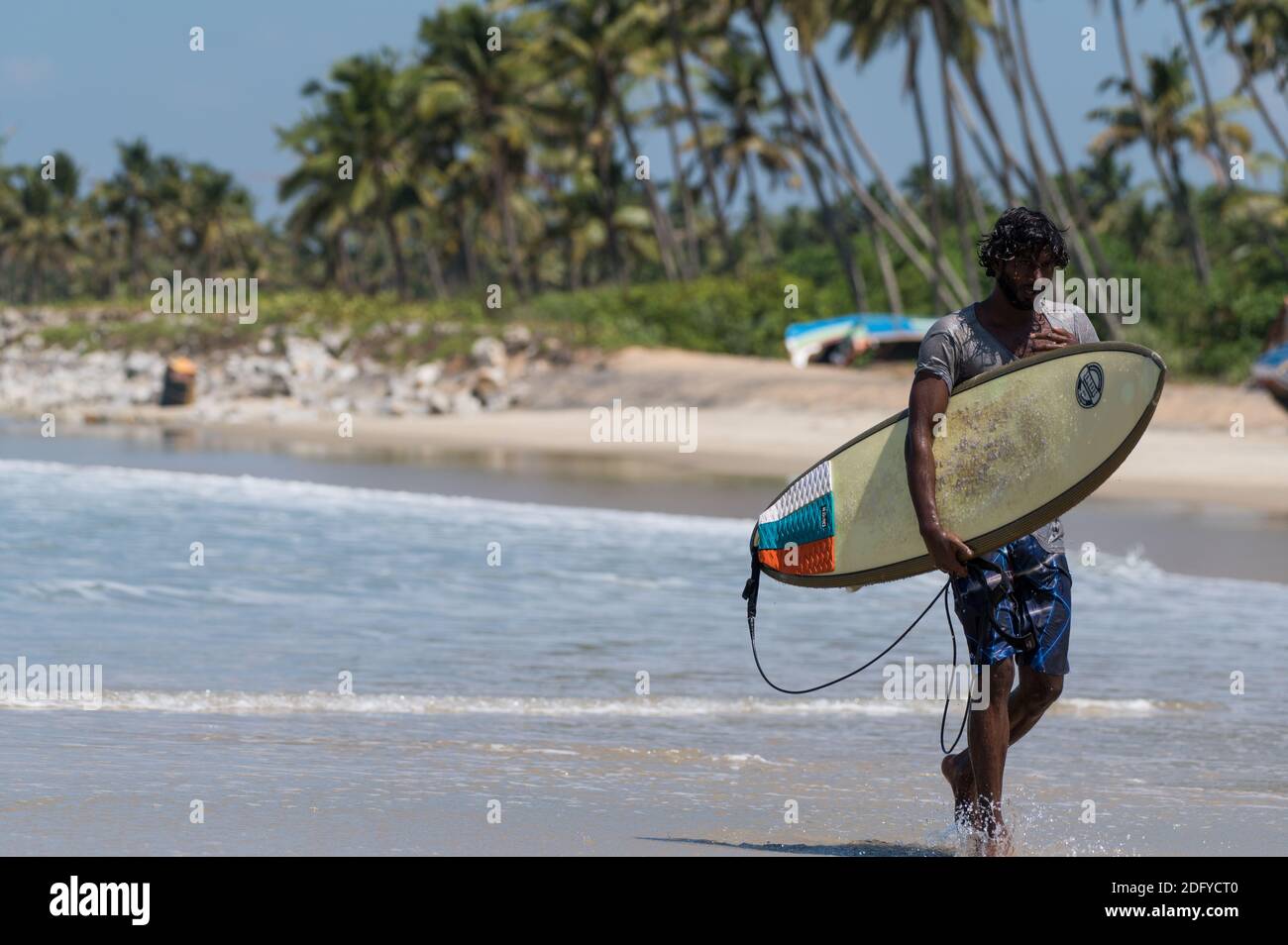 VARKALA, INDIA - 14 marzo 2020: Un maschio indiano con la sua tavola da surf che cammina vicino alla costa del mare Foto Stock