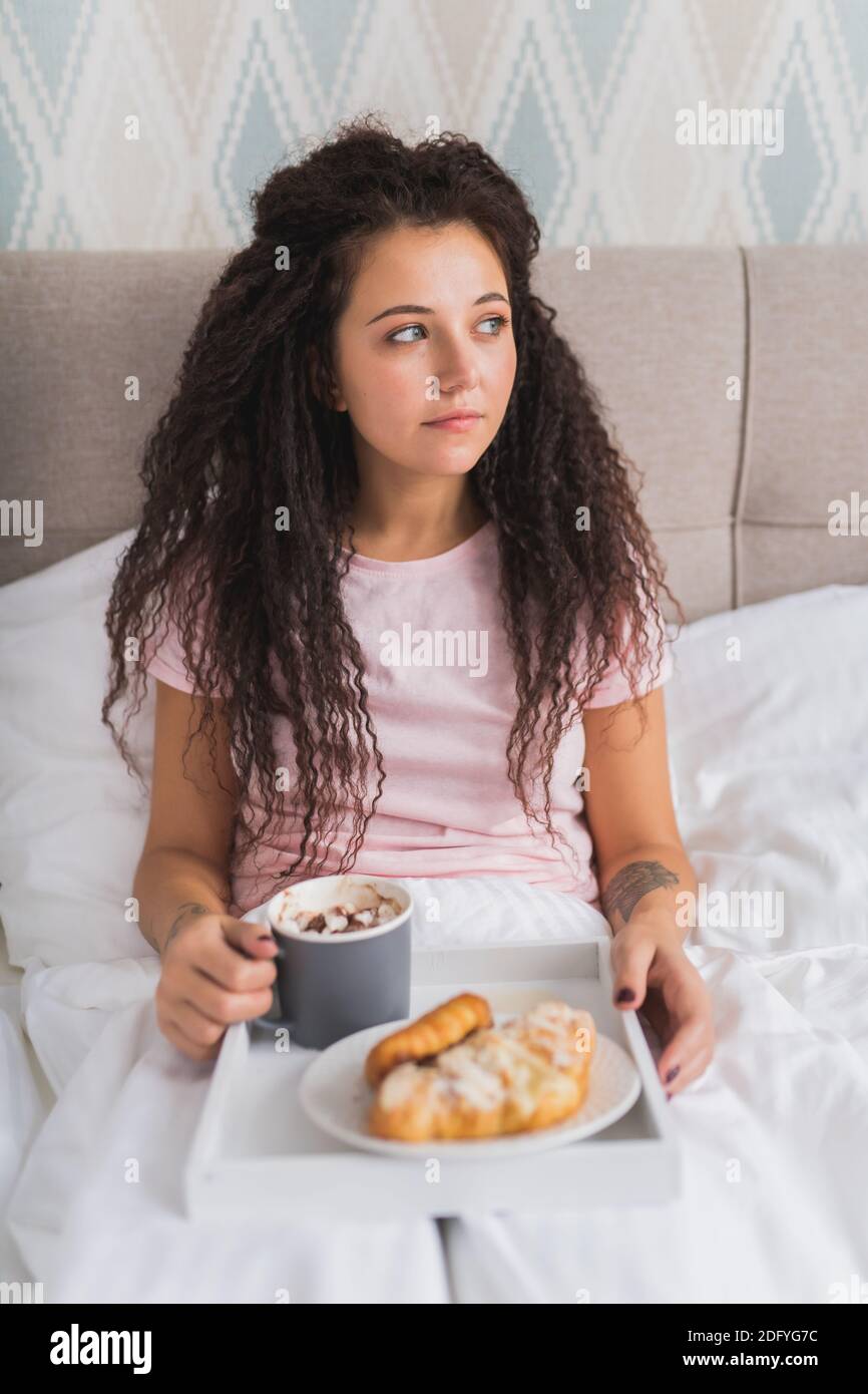 La giovane donna adulta felice fa colazione a casa adagiandosi sul tappeto  e mangiando dolci biscotti con caffè e latte sorridendo alla macchina  fotografica in una allegra pezza Foto stock - Alamy