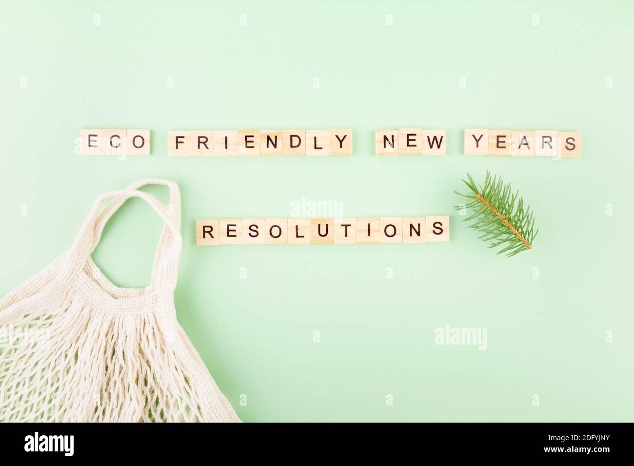 Frase 'le risoluzioni del nuovo anno eco-friendly' in lettere di legno su sfondo verde, borsa a corda e rami di abete Foto Stock