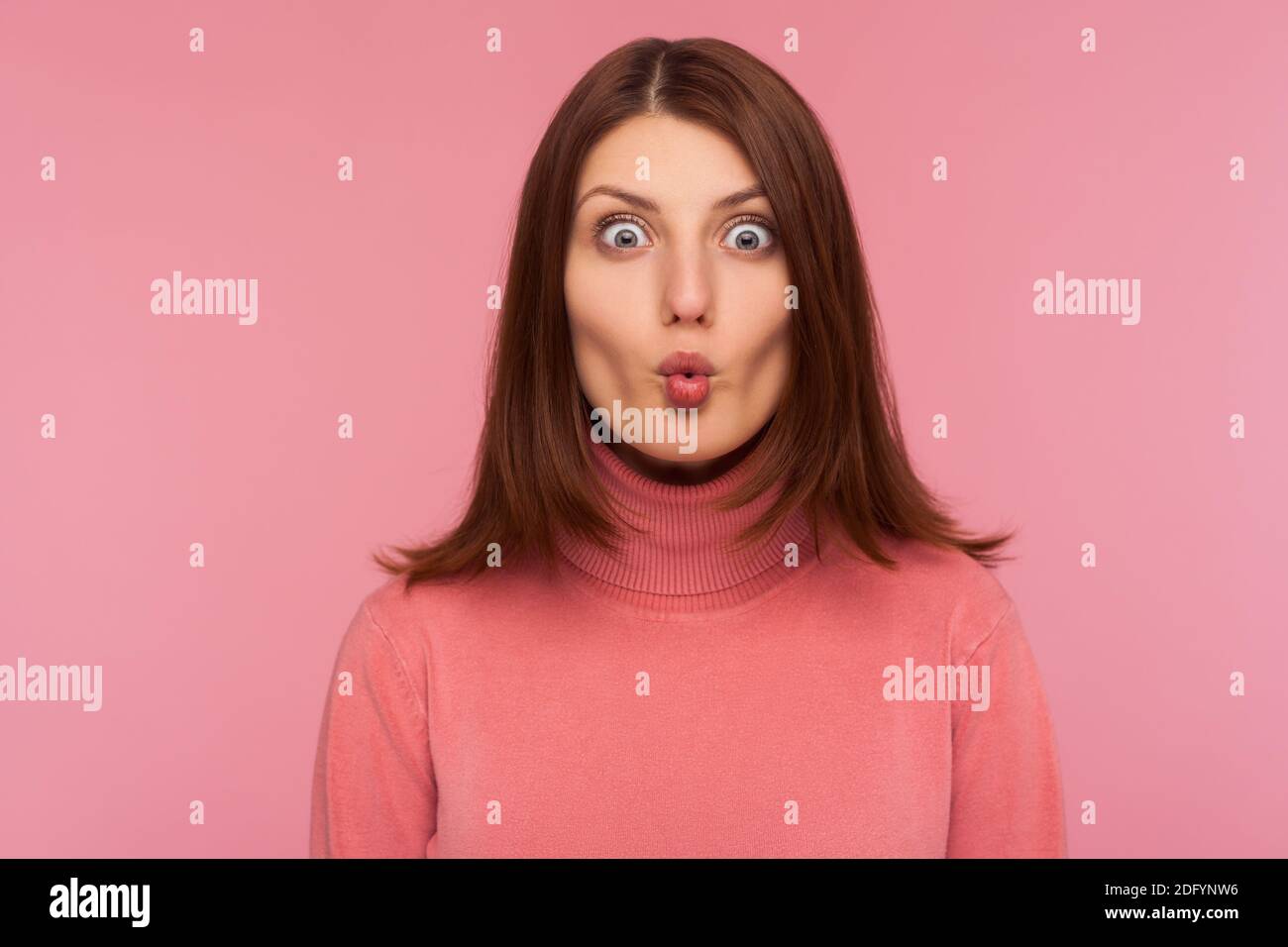 Closeup ritratto attraente donna brunette in rosa maglione ingannare intorno a fare labbra di pesce, avendo divertimento, umorismo. Studio al coperto isolato su bac rosa Foto Stock