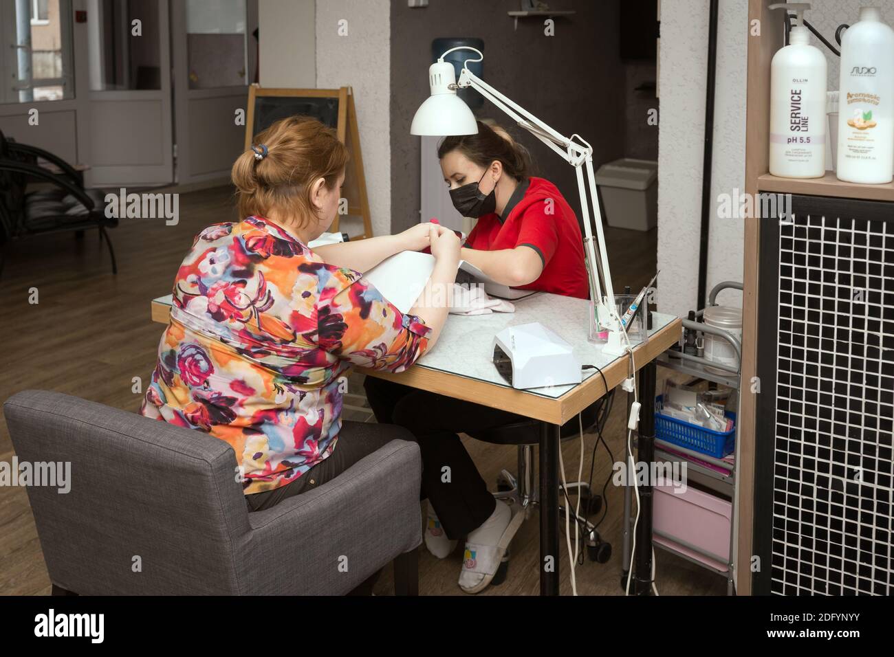 Un tecnico professionale del chiodo fa un manicure per un cliente ad un tavolo di lavoro in un salone dei capelli e delle unghie. Foto Stock