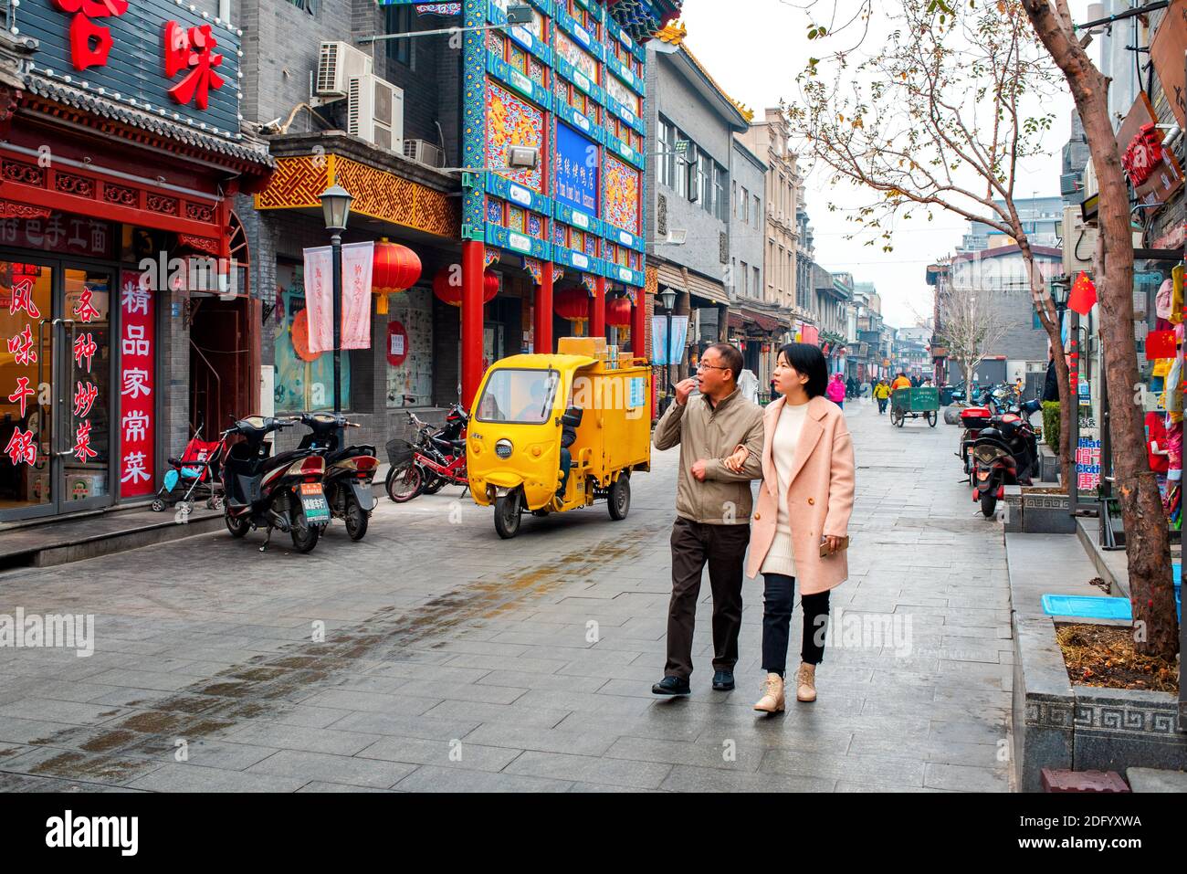 I turisti asiatici camminano lungo la strada turistica principale nel quartiere storico di Hutong a Pechino. Risciò automatico giallo su sfondo. Marcia lenta. Foto Stock