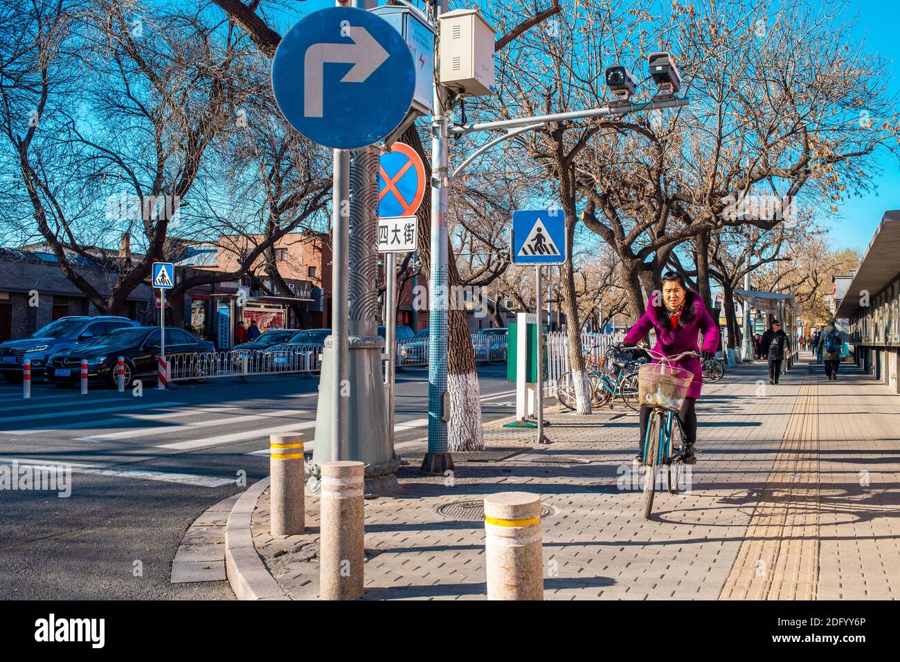 Una donna cinese corre in bicicletta lungo una strada nel centro della città. Stile di vita cittadino e scene di strada. Mattina soleggiata autunno a Pechino. Foto Stock