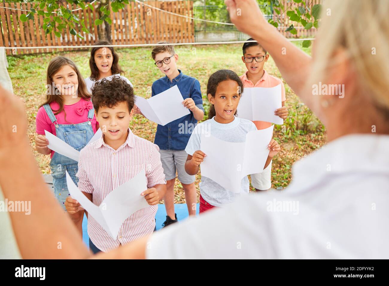 Insegnante di musica pratica una canzone con il coro dei bambini per la mostra di talenti nel campo estivo Foto Stock