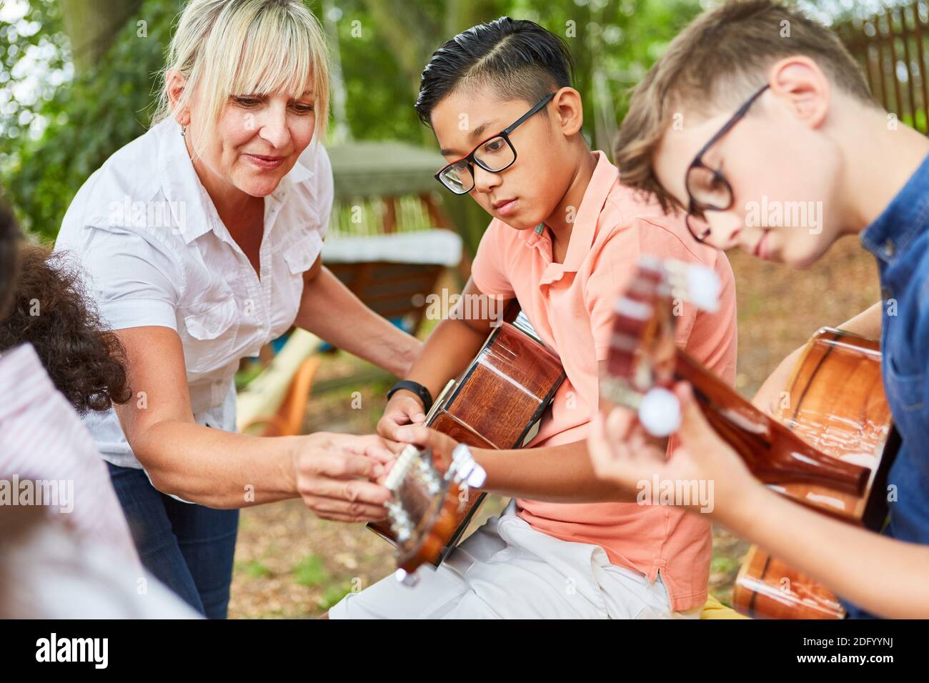 Insegnante aiuta i bambini in lezioni di chitarra nel campo estivo prima talent show Foto Stock