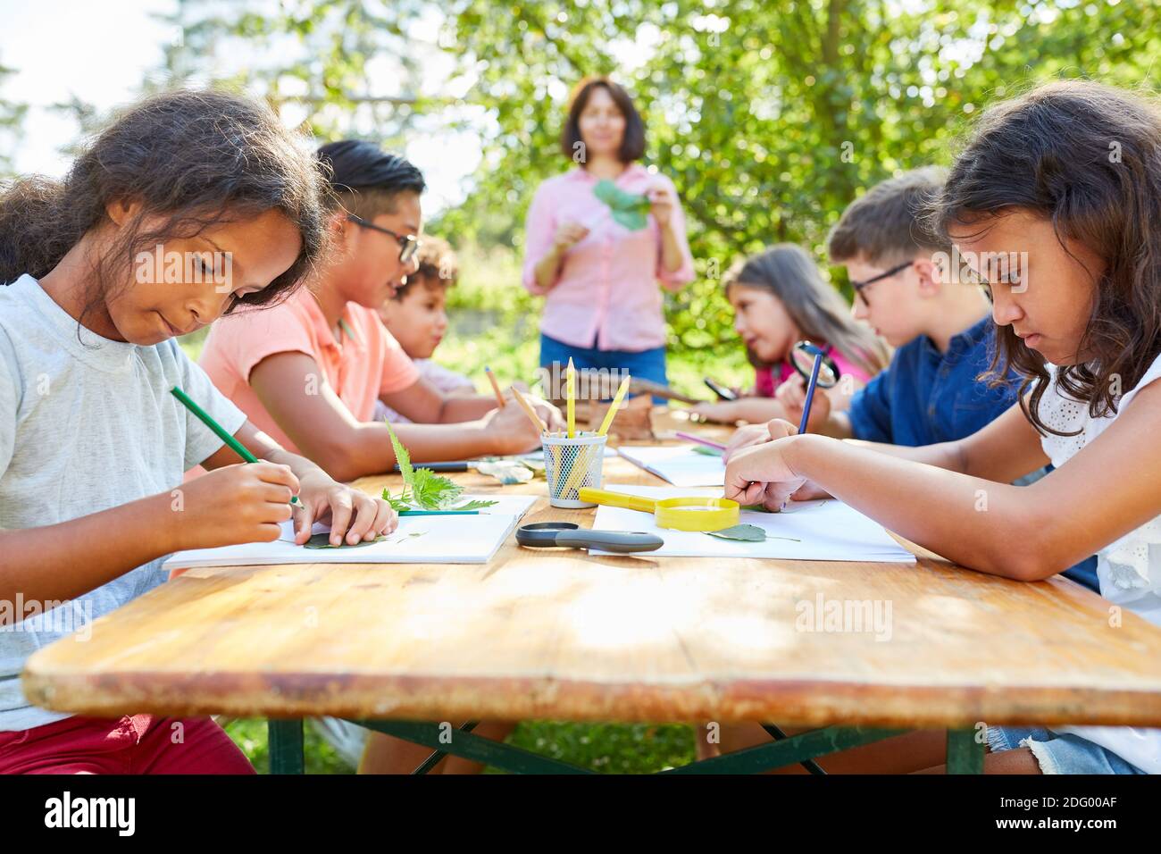 Gruppo di bambini concentrati nel disegno e nel fare del campo estivo artigianato con foglie Foto Stock