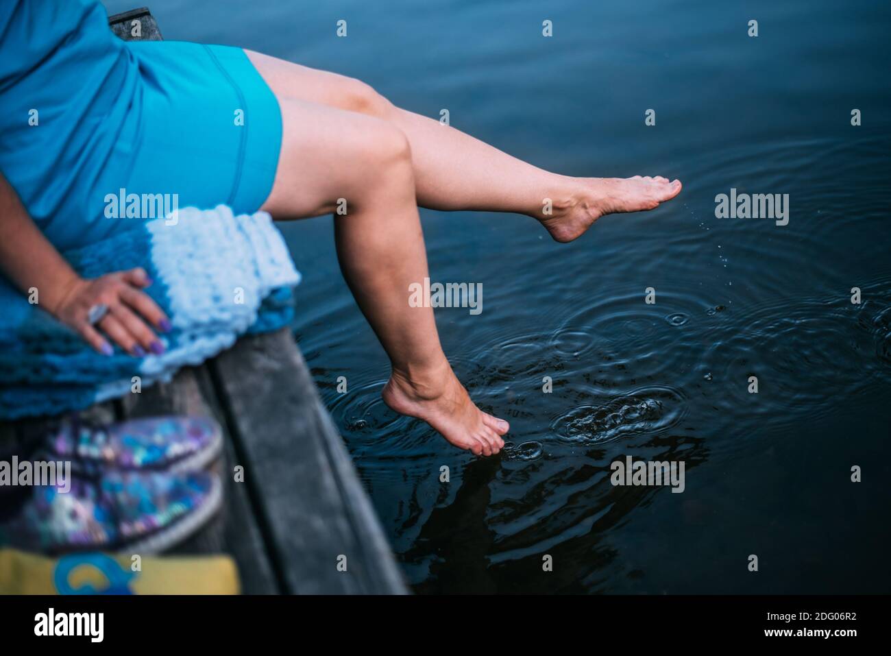 donna seduta su un ponte di legno vicino all'acqua, le gambe penzolate e tocca la superficie dell'acqua Foto Stock