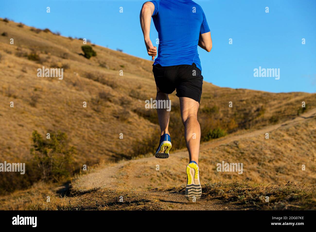 indietro uomo corridore correre sentiero di montagna su sfondo cielo blu Foto Stock