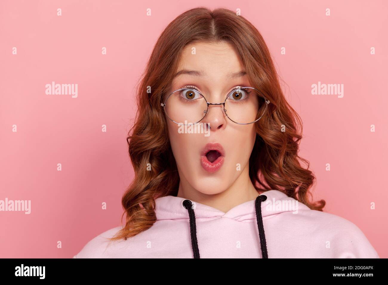 Ritratto di giovane adolescente sorpreso femmina in occhiali rotondi guardando la macchina fotografica con bocca aperta, gesturing wow, sentirsi felice o scioccato. Stu. Interno Foto Stock
