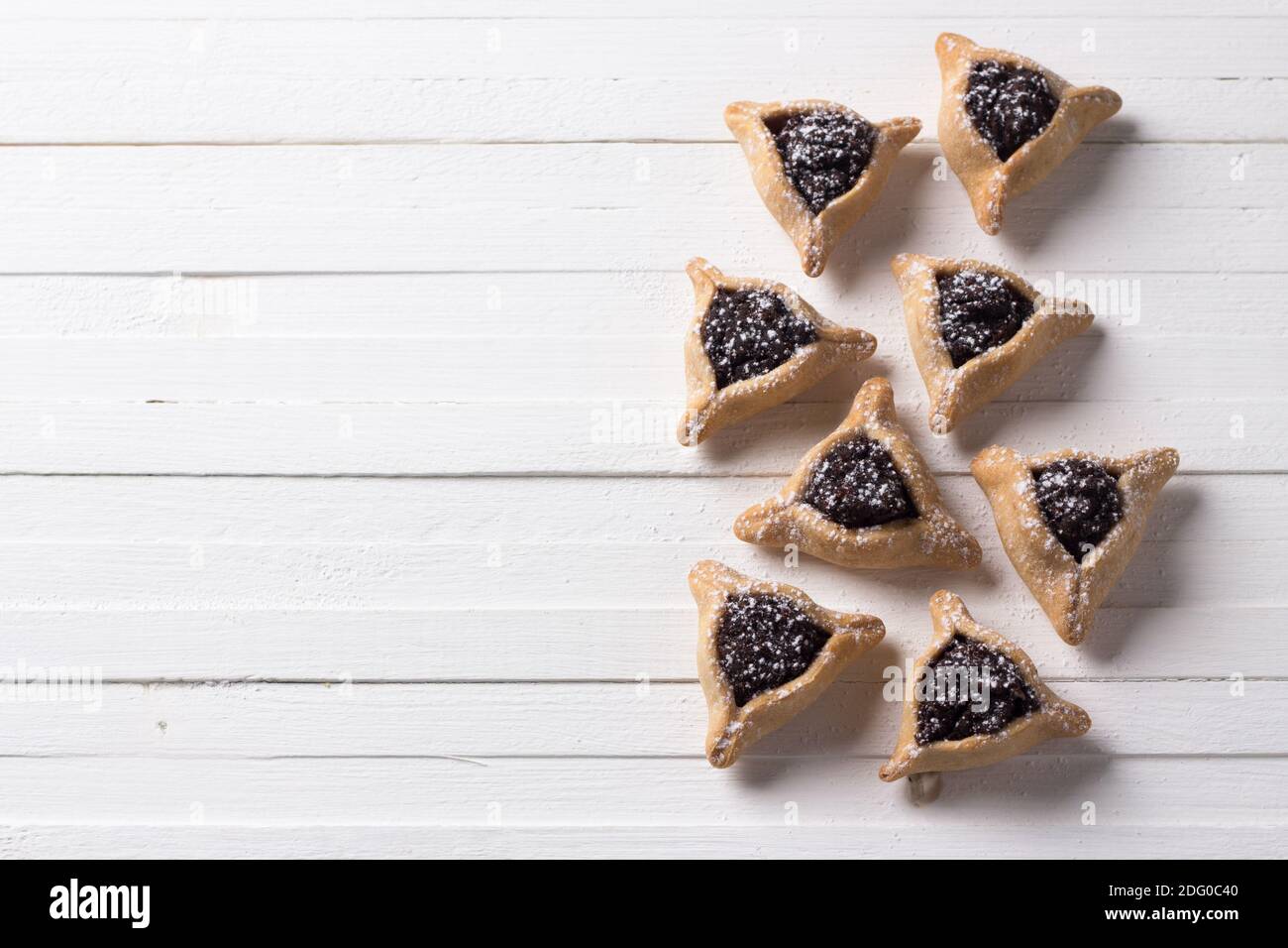 Dolci tradizionali per la vacanza ebraica Purim. Biscotti Hamantashen o orecchie di Haman, biscotti triangolari con semi di papavero e uvetta su una parte posteriore bianca Foto Stock