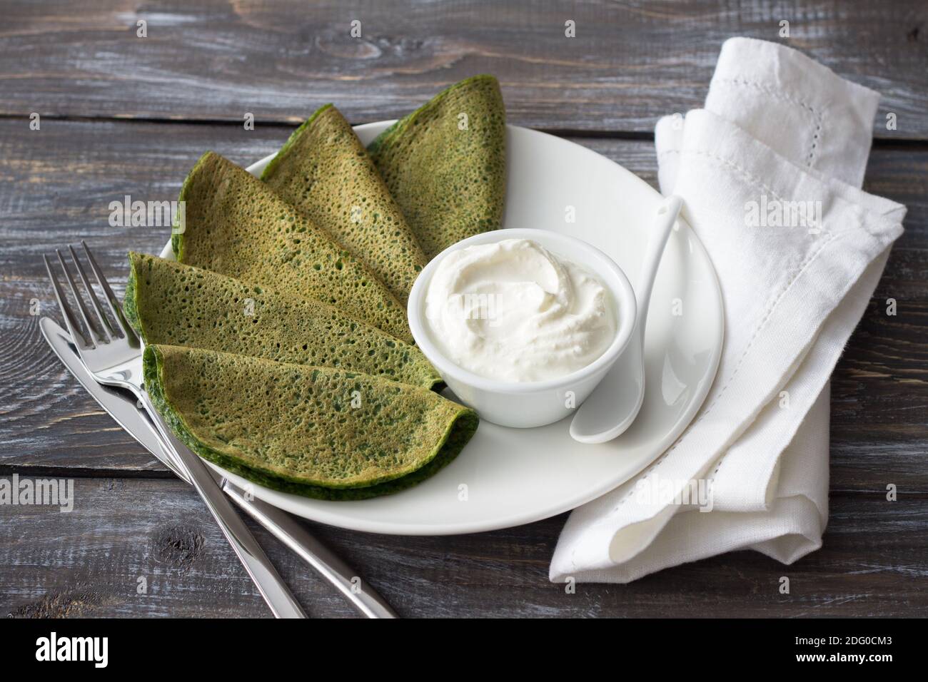 Frittelle di spinaci con salsa al formaggio su un piatto bianco su un tavolo di legno. Deliziosa colazione sana Foto Stock