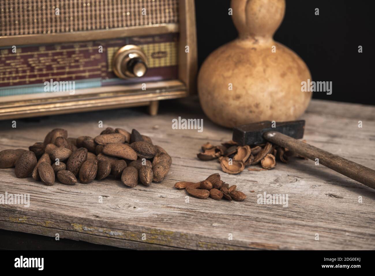 primo piano di tavolo di legno chiaro con sfondo scuro, vecchia radio e zucca secca sullo sfondo e mandorle con martello per sbucciarle Foto Stock