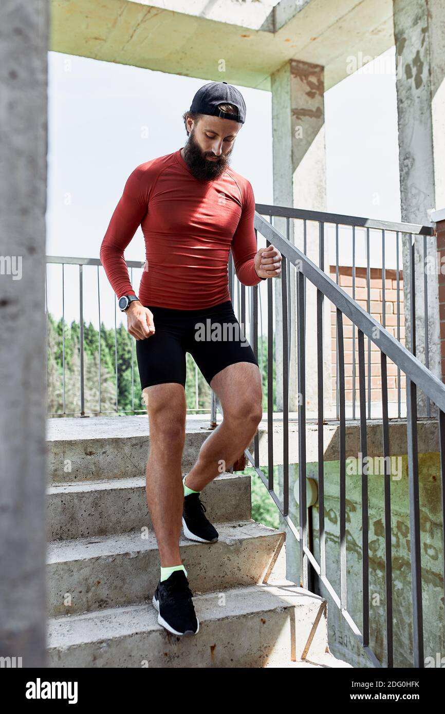 Atleta maschile concentrato che corre sulle scale per rendere l'allenamento più intensivo. Sportivo bello giovane uomo allenarsi da solo all'aperto. Punto di allenamento per scale Foto Stock