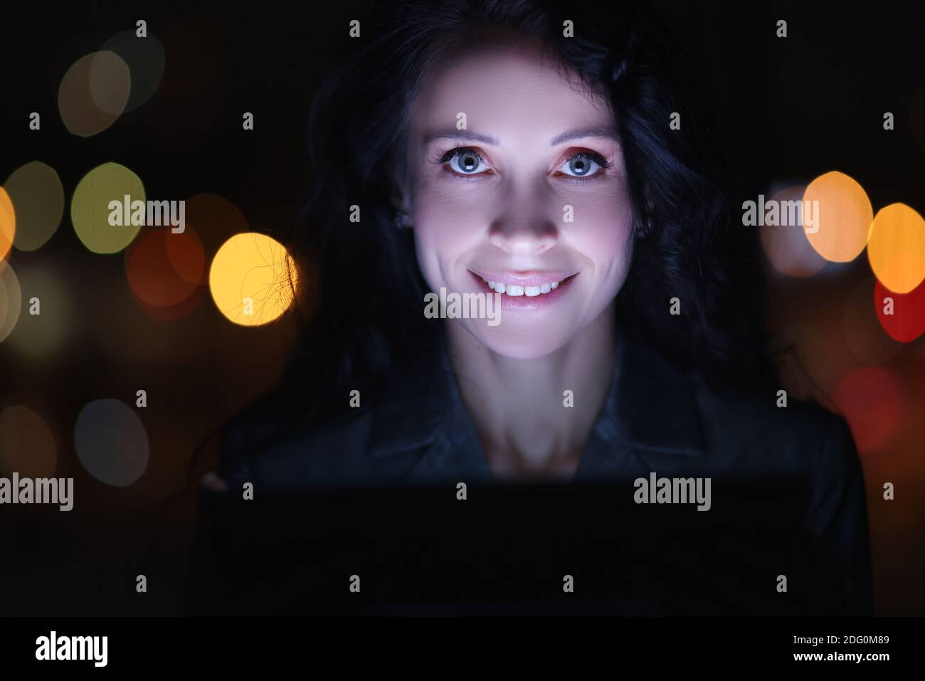 Ritratto di donna brunetta al computer portatile di notte sullo sfondo di ghirlande Foto Stock