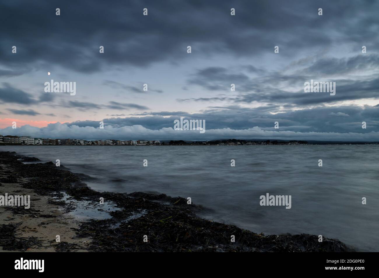 Una linea di soffici nuvole bianche come le montagne sovrasta i piccoli edifici di Sandbanks, mentre l'acqua calma e grigia lambisce la riva. Foto Stock