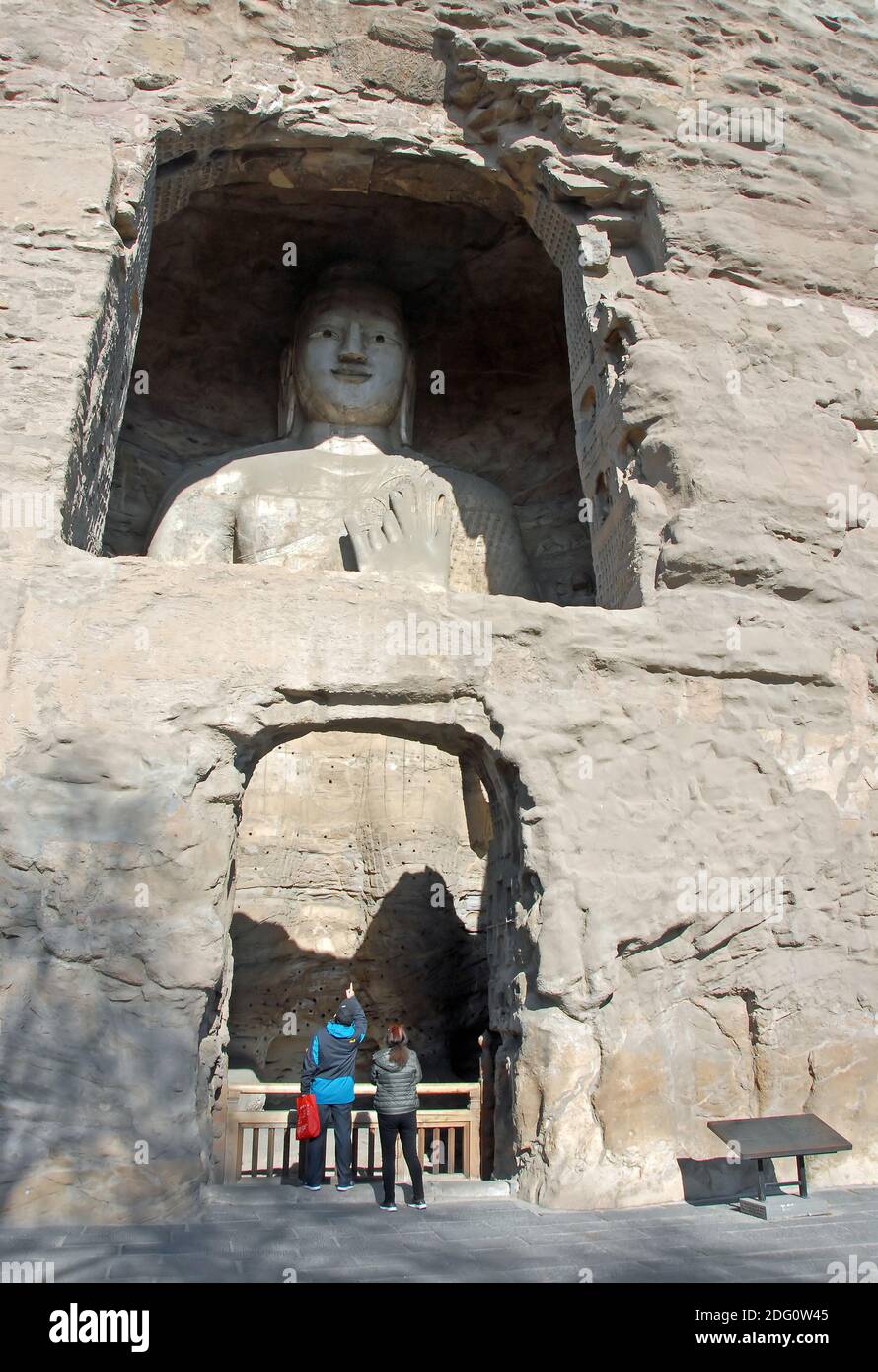 Grotte di Yungang vicino a Datong nella provincia di Shanxi, Cina. Grande statua di Buddha in una grotta a Yungang. Buddha in piedi con persone irriconoscibili. Foto Stock