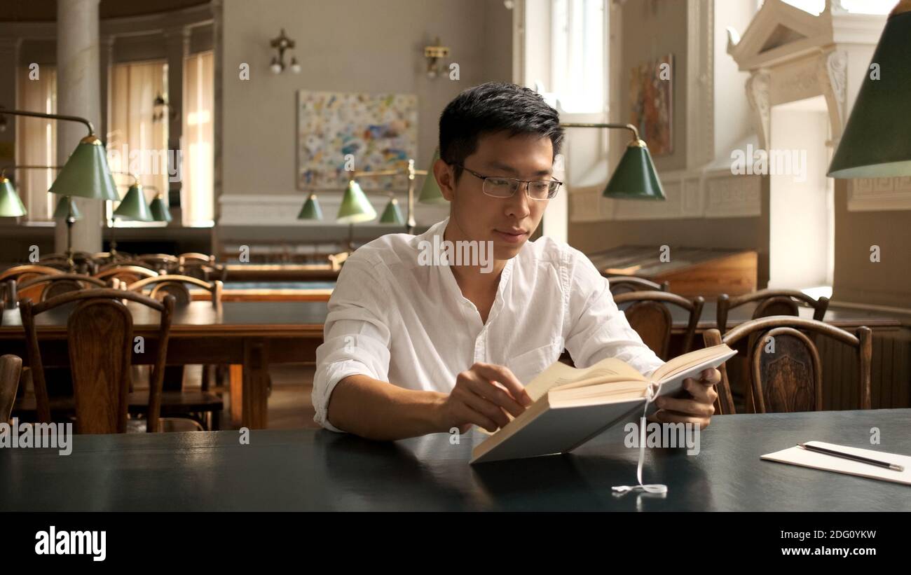 Giovane studente asiatico maschio che studia con attenzione con il libro di testo e la preparazione per esami in libreria Foto Stock