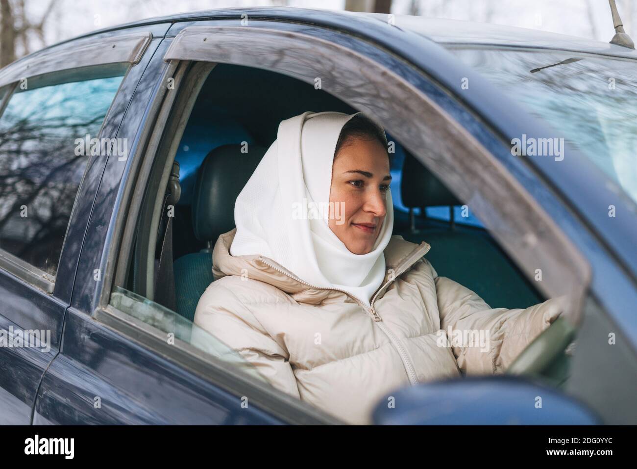 Bella giovane donna musulmana sorridente in foulard in abiti leggeri in auto con guida a destra Foto Stock