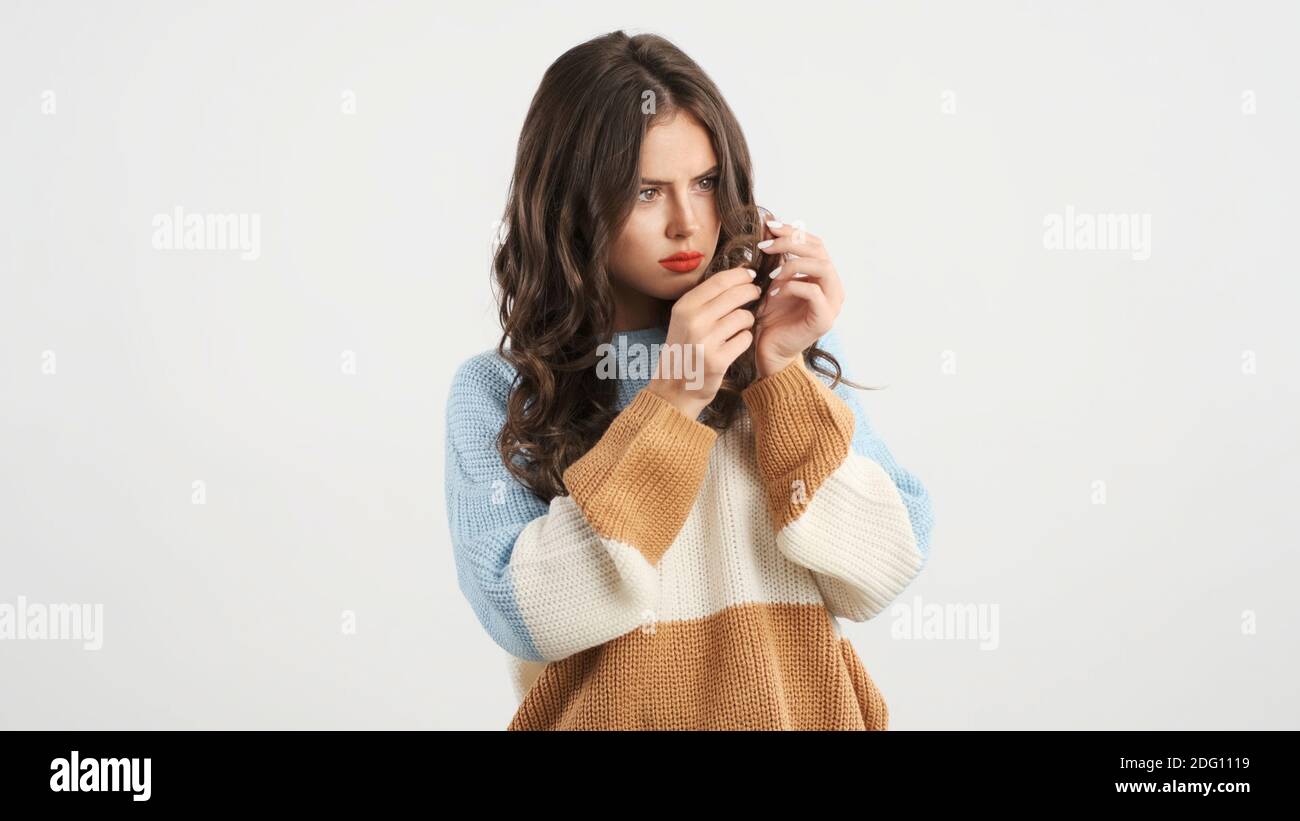Attraente ragazza stupita in maglione pensando di tagliare i capelli suggerimenti su sfondo bianco Foto Stock
