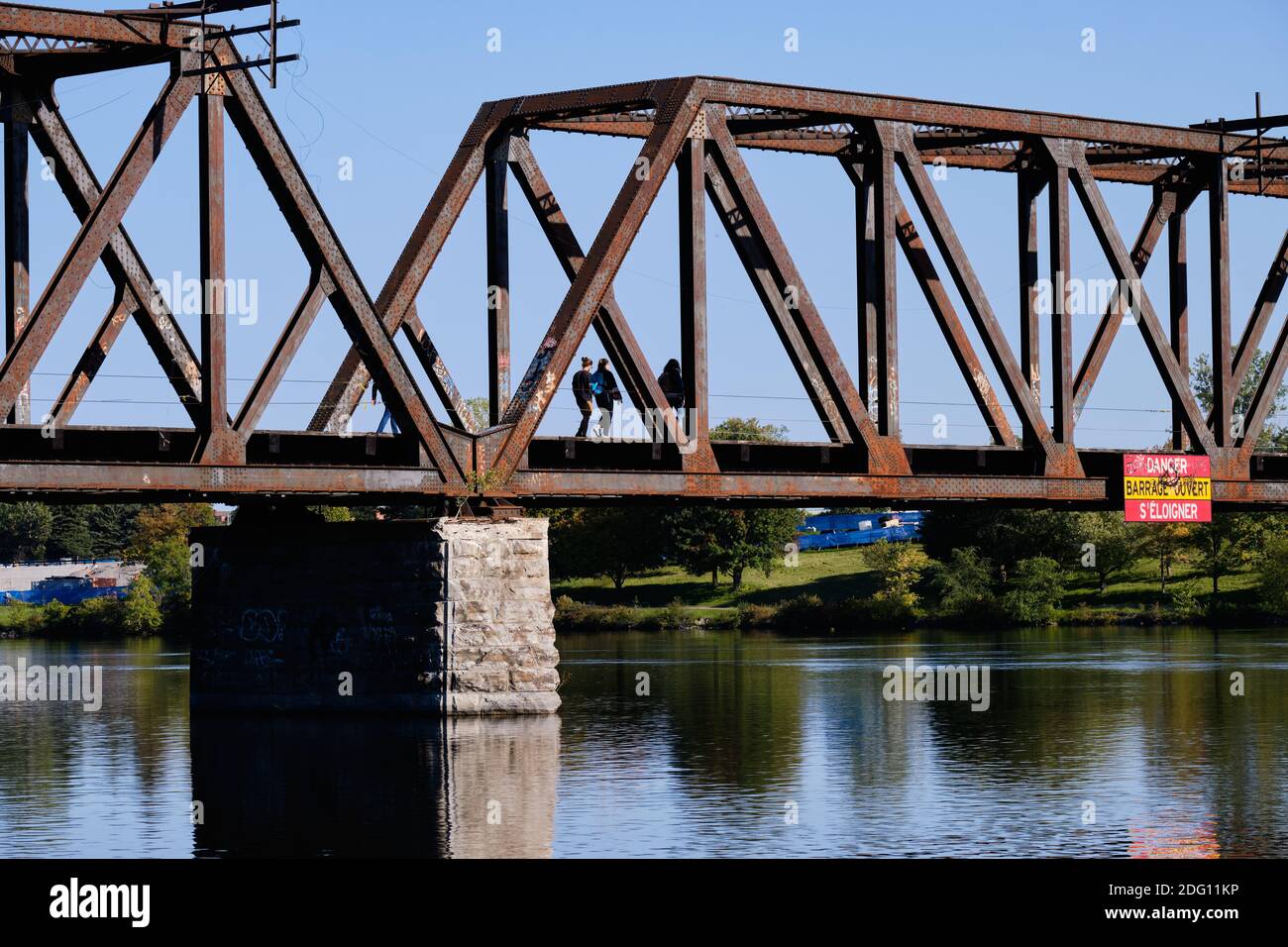 Adolescenti visti da dietro a piedi su vecchio treno arrugginito disusato ponte sul fiume Foto Stock
