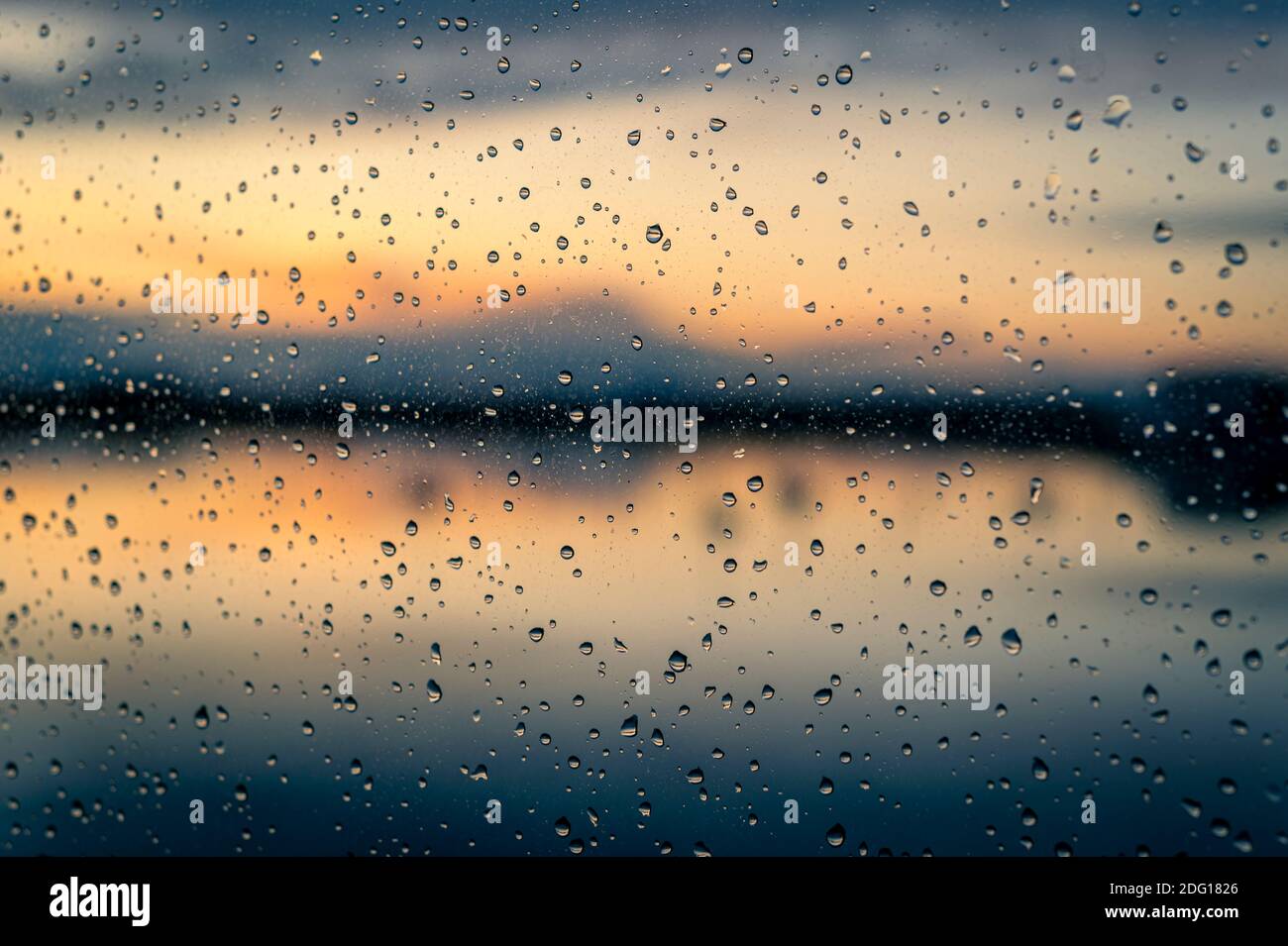 Primo piano di gocce di pioggia su una finestra con un tramonto attraverso l'acqua sullo sfondo Foto Stock
