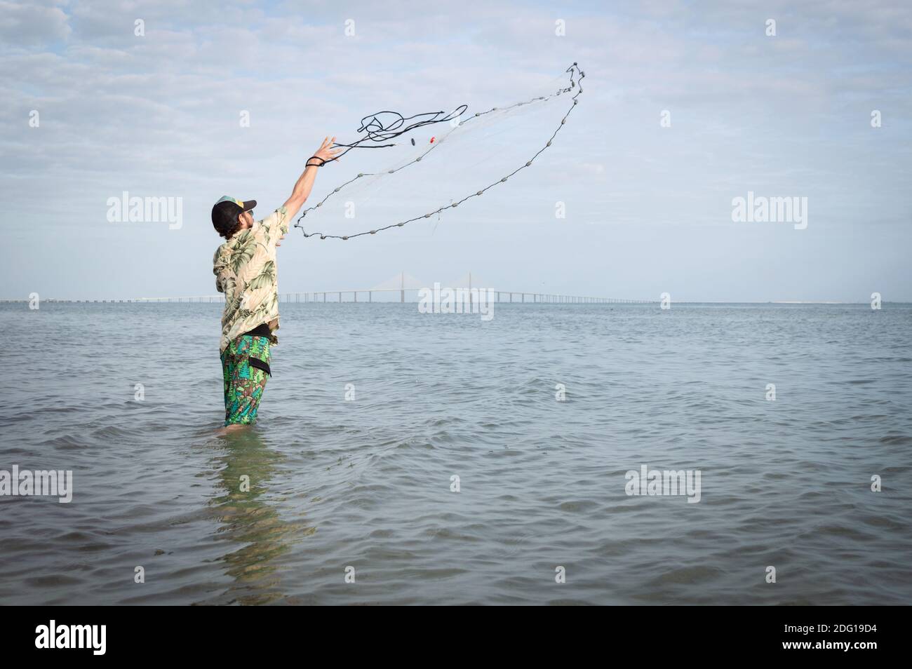 Clearwater, Florida / USA : 18 Jan 2020: Un uomo si erge a vita profonda e getta una rete da pesca nella baia di Tampa al Fort desoto state Park in una giornata di sole. Foto Stock