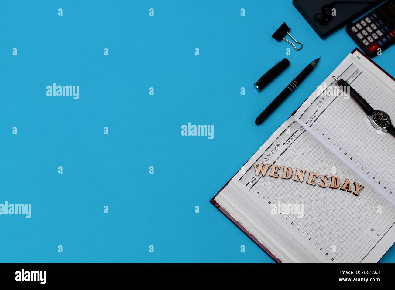 Moderna scrivania da ufficio con notebook, penna e materiali di consumo vuoti. Copiare lo spazio su sfondo blu. Vista dall'alto. Stile di posa piatto. Lettering mercoledì Foto Stock