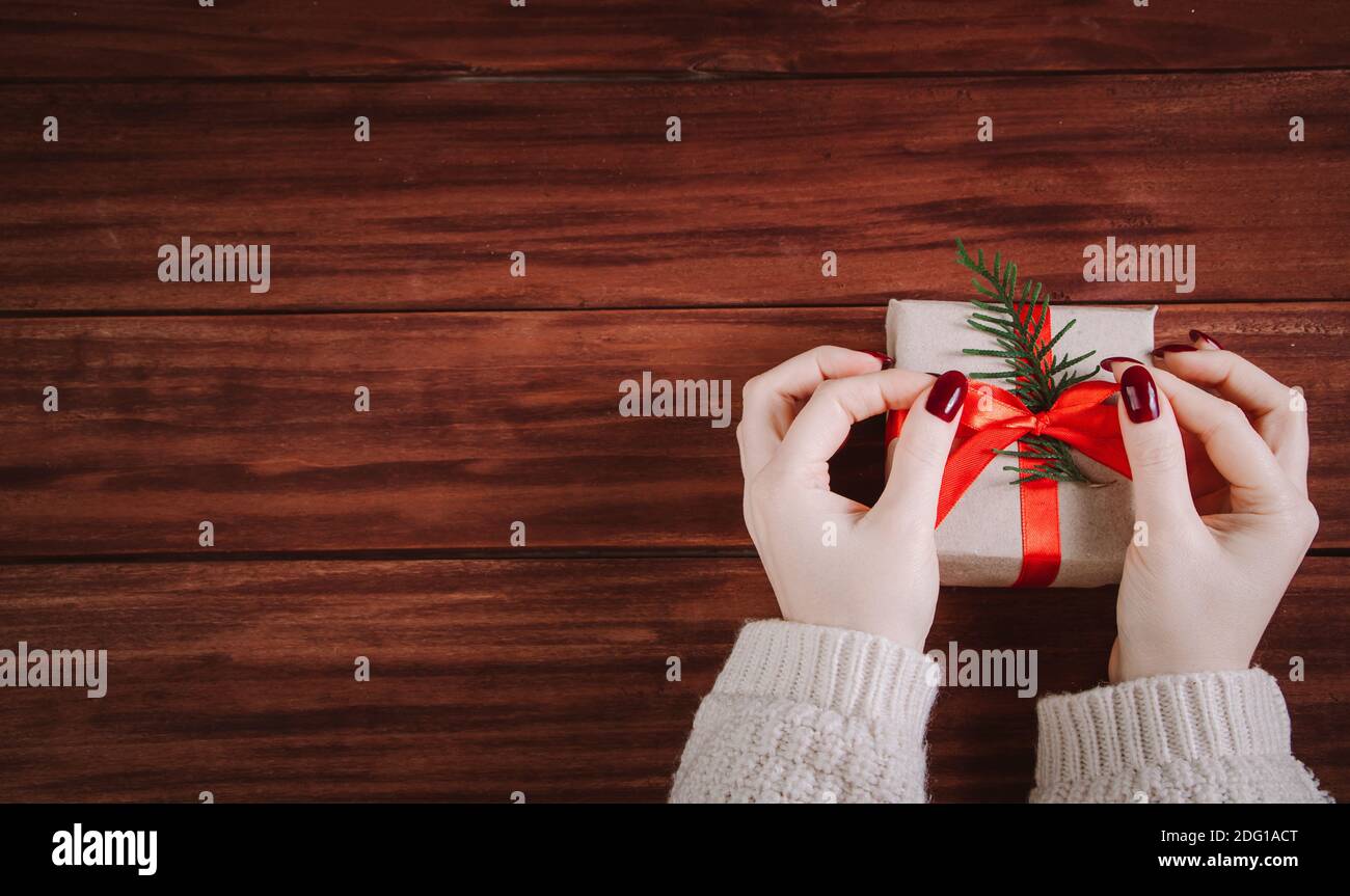 Processo di confezionamento regalo di Natale. Donna decora scatola con nastro rosso. Foto Stock