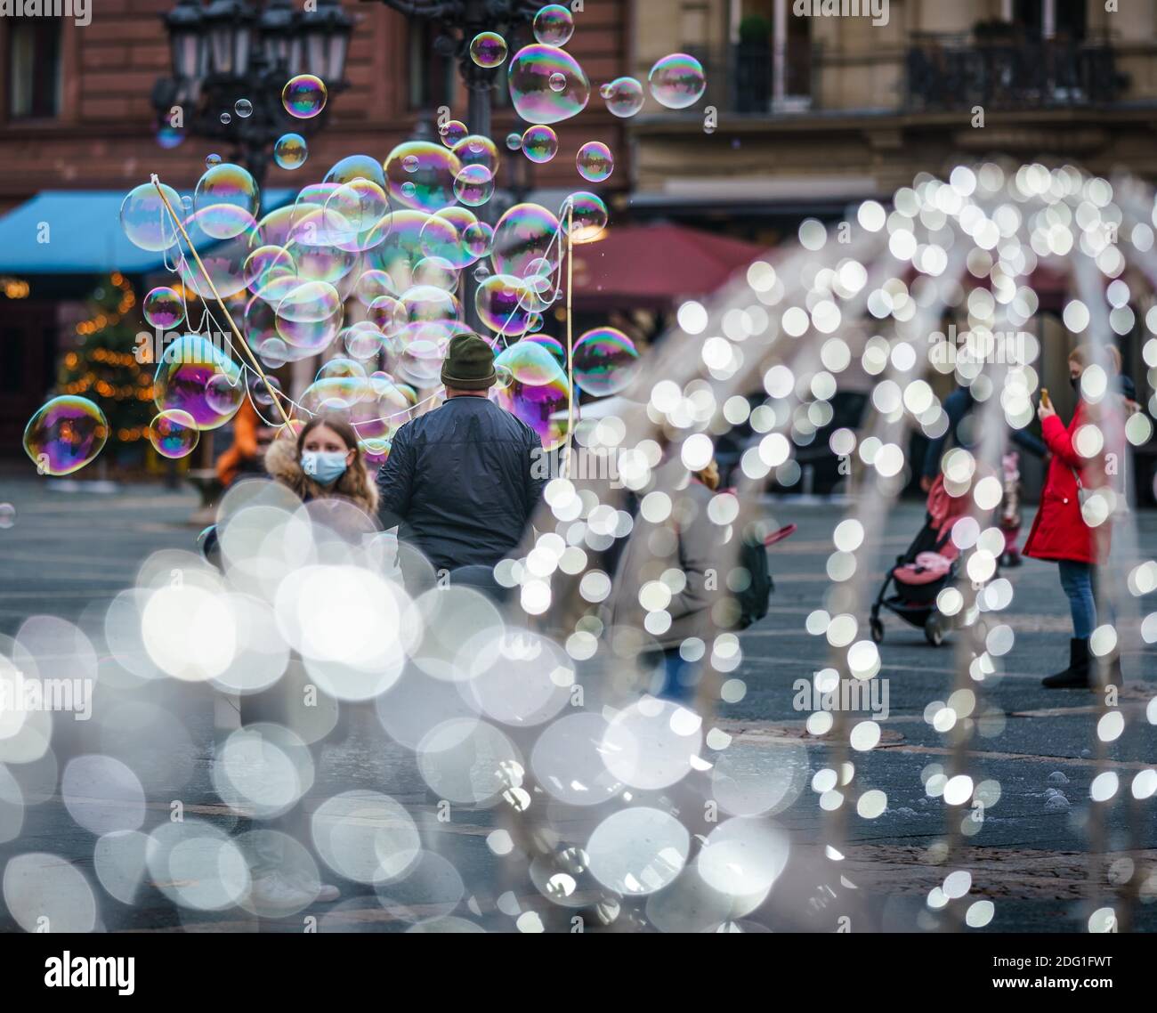 07 dicembre 2020, Hessen, Francoforte sul meno: Un artista di strada fa lievitare grandi bolle di sapone, mentre in primo piano le luci dell'illuminazione natalizia nella fontana sulla piazza dell'opera brillano. Foto: Frank Rumpenhorst/dpa Foto Stock