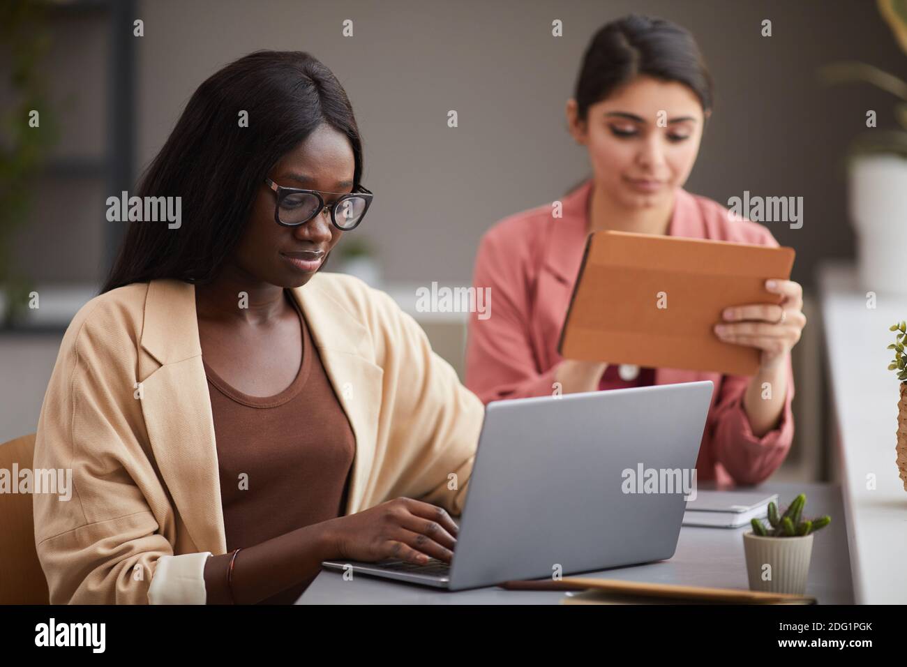 Ritratto di una donna d'affari afroamericana contemporanea che usa un computer portatile alla scrivania mentre gestisce un'azienda di successo con una partner femminile, spazio di copia Foto Stock