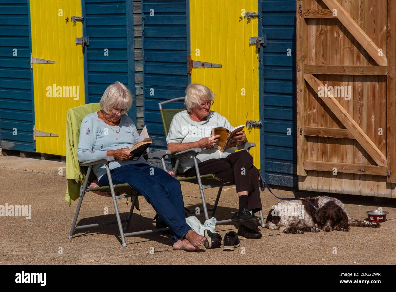 Godendo il sole e leggendo in una sedia a sdraio fuori di una capanna sulla costa del Kent vicino a Margate, Thanet, Inghilterra Foto Stock