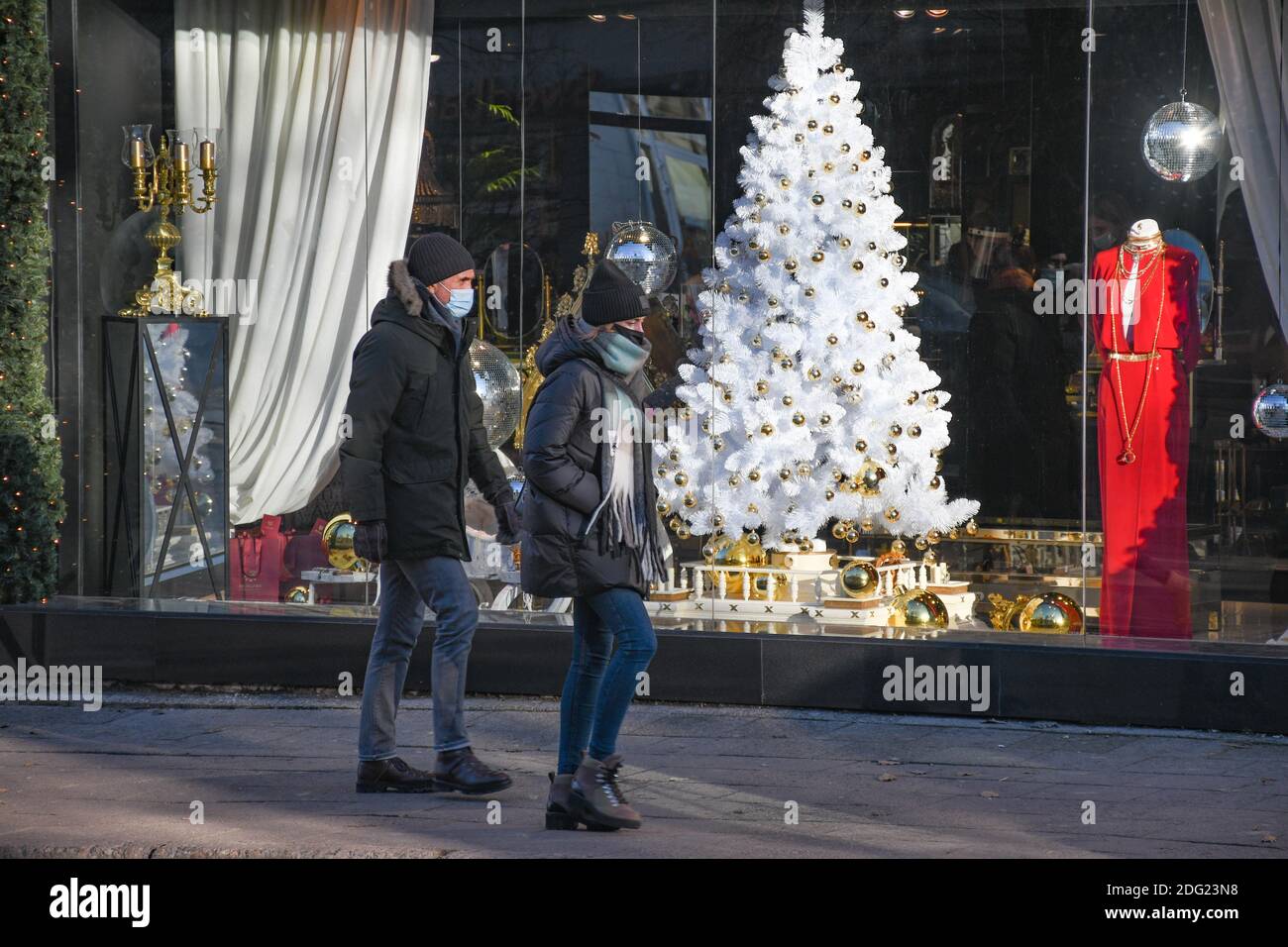 Coppia che indossa maschere protettive che camminano in città vicino a un negozio o centro commerciale durante Natale, Covid o Coronavirus focolaio Foto Stock