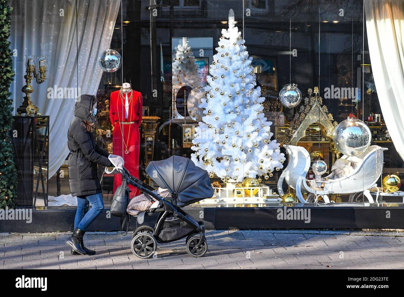 Ragazza con passeggino a piedi in città vicino a un negozio o centro commerciale durante Covid o Coronavirus focolaio, sfondo di Natale Foto Stock