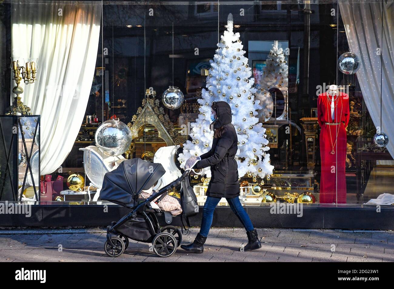 Ragazza con passeggino a piedi in città vicino a un negozio o centro commerciale durante Covid o Coronavirus focolaio, sfondo di Natale Foto Stock